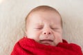 Top View Portrait First Days Of Life Newborn Funny Sleeping crying face close Baby child Wrapped In Red Diaper At White