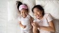 Overjoyed Asian young mum and small daughter lying in bed Royalty Free Stock Photo