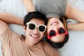 Top view portrait shot of a romantic young Asian lover couple cute smiling wearing stylish modern sunglasses, lying on the bed and Royalty Free Stock Photo