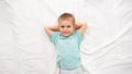 Top view portrait of smiling little boy lying on white sheets on the bed and looking in the camera. Concept of happy Royalty Free Stock Photo