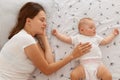 Top view portrait of woman sleeping with her small daughter on bed, mommy lying with infant girl swearing white t shirt, happy