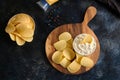 Top view potato chips, sauce in a white bowl, peppers on a wooden cutting board