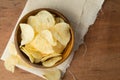 Top view of potato chips in wooden bowl putting on linen and wooden background