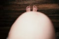 Top view of a pregnant woman's belly standing shoeless on the floor