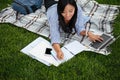 Top view of pretty asian student, keeping records in paper notebook while studying online with laptop, lying on checkered Royalty Free Stock Photo