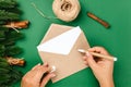 top view, process of writing letter to Santa Claus on craft envelope on green table with decorations of Christmas trees