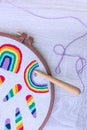 Top view of punch needle making a violet row of a rainbow on grey fabric in embroidery hoop and violet thread on white wooden Royalty Free Stock Photo