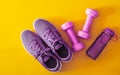 Top view of purple and violet sport shoes, dumbbells and bottle of water on yellow background. Fitness and Healthy lifestyle