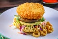 Top view of a Ramen burger with a crispy shrimp patty and wasabi mayo on a colorful plate