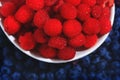 Top view of raspberries in the plate on background of blueberries. Fresh berries assortment. Ripe and juicy fresh raspberries