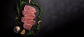 Top view of raw beef steak lying on a dark background. Piece of meat on chalkboard, schist stone. Spices and herbs around.