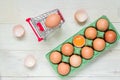 Top view of raw brown chicken eggs in green egg carton box and shopping cart on white wooden background Royalty Free Stock Photo