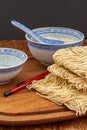 Top view of raw noodles with rice bowl, chopsticks on wooden board and dark background Royalty Free Stock Photo