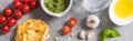 Top view of raw Pappardelle near tomatoes, garlic, basil, pine nuts, olive oil, water and pesto sauce on grey surface, panoramic Royalty Free Stock Photo