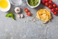 Top view of raw Pappardelle near tomatoes, garlic, basil, pine nuts, olive oil, water and pesto sauce on grey surface Royalty Free Stock Photo