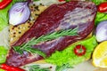 Top view of raw red beef meat with green rosemary and fresh vegetables on light wooden cutting board background. Royalty Free Stock Photo