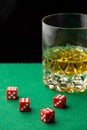 Top view of red dice on green baize with glass of whiskey, defocused, black background Royalty Free Stock Photo