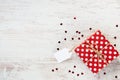 Top view of a red dotted gift box over white wood background. Copy space. Empty note.