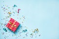 Top view of a red dotted gift box, scattered glittering star shaped confetti and colorful ribbons over blue background. Celebratio Royalty Free Stock Photo