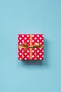 Top view of a red dotted gift box tied with golden bow over blue background.