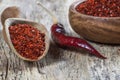 Top view red dried crushed hot chili peppers and chili flakes or powder in wooden spoon and bowl on wooden rustic background Royalty Free Stock Photo