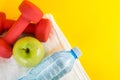 Top view of red dumbbells, green apple and fresh water bottle with dew on white towel and yellow space Royalty Free Stock Photo