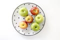 Top view of Red and green apples in white plate with black triangles pattern on white background