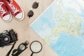 Top view of red gumshoes, film camera, magnifier, compass, sunglasses and world map on wooden surface.