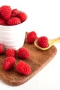 Top view of red raspberries in a white bowl on wooden board, one in a wooden spoon Royalty Free Stock Photo