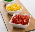 Top view of red, yellow, and peppers cut into cubes in white saucers on a wood cutting Royalty Free Stock Photo