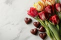 Top view of red and yellow tulips and chocolate heart shaped candies lying on light background. Royalty Free Stock Photo