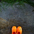 Top view of reddish rubber boots on wet concrete background in front of the wet green grass Royalty Free Stock Photo