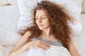 Top view of relaxed curly woman has healthy sleep in bed, lies on white linen, enjoys pleasant dreams at night, peaceful atmospher Royalty Free Stock Photo