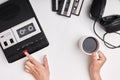 Top view of retro tape recorder, cassettes and headpnones lying on white surface. Woman`s hands switcing on old tape recorder list Royalty Free Stock Photo