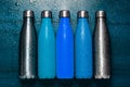 Top view of reusable stainless thermos bottles, sprayed with water on wooden table. Hue of blue color.