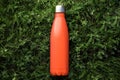 Top view of reusable steel thermo water bottle with mockup on green grass, lush lava color.