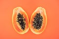 Top view of ripe bright papaya halves with black seeds isolated on orange.