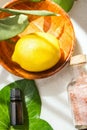 Top View Ripe Yellow Lemon in Wooden Bowl Essential Oil Bottle on Green Ivy Leaves Pink Himalayan Salt on White Marble. Bright Sun