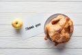 Top view of roasted turkey, apple and card with thank you lettering served on white wooden table.