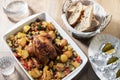 View of a rotisserie chicken with baked potatoes and assorted vegetables on a baking dish with bread on a wooden table Royalty Free Stock Photo