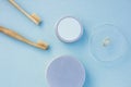 Top view of round silver cans, bamboo toothbrushes, glass cup with tooth paste smudge on pastel blue background. Zero waste