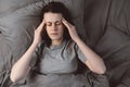 Top view of sad unhealthy young woman lying down on bed in living room at home with closed eyes, holding head with hand Royalty Free Stock Photo