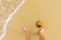 Top view of sand beach with a sea wave, men`s feet and coconut Royalty Free Stock Photo