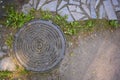 Top view of sand, grass, paved path and manhole in the rays of the rising sun