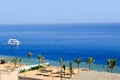 Top view of a sandy beach with sunbeds and sun umbrellas and two large white ships, a boat, a cruise liner floating in the sea on Royalty Free Stock Photo