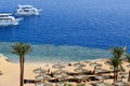 Top view of a sandy beach with sunbeds and sun umbrellas and two large white ships, a boat, a cruise liner floating in the sea on Royalty Free Stock Photo