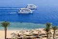 Top view of a sandy beach with sunbeds and sun umbrellas and two large white ships, a boat, a cruise liner floating in the sea on Royalty Free Stock Photo
