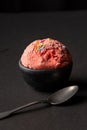 Top view of scoop of strawberry ice cream in black bowl with spoon