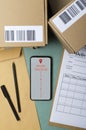 Top view of screen of mobile phone and order tracking map on it, parcels with bar codes, clipping board and delivery form on the t