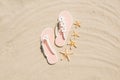 Top view of sea stars and white woman flip flops with flowers on sandy beach. Summer vacation concept on a sunny day Royalty Free Stock Photo